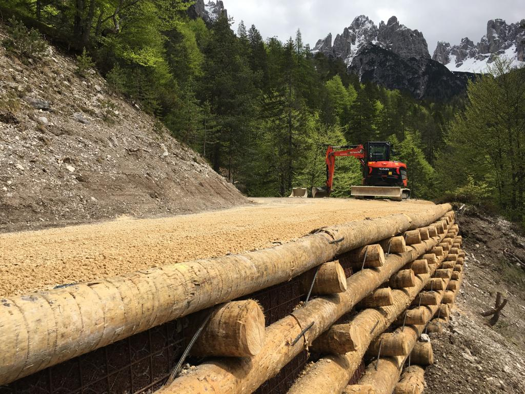 Italian La foto mostra un cantiere di costruzione di un terrapieno lungo una strada in una zona montuosa. Un escavatore ro...